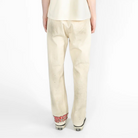 A model viewed from the back, wearing a cream-colored shirt and matching cream trousers, standing against a plain white studio background.