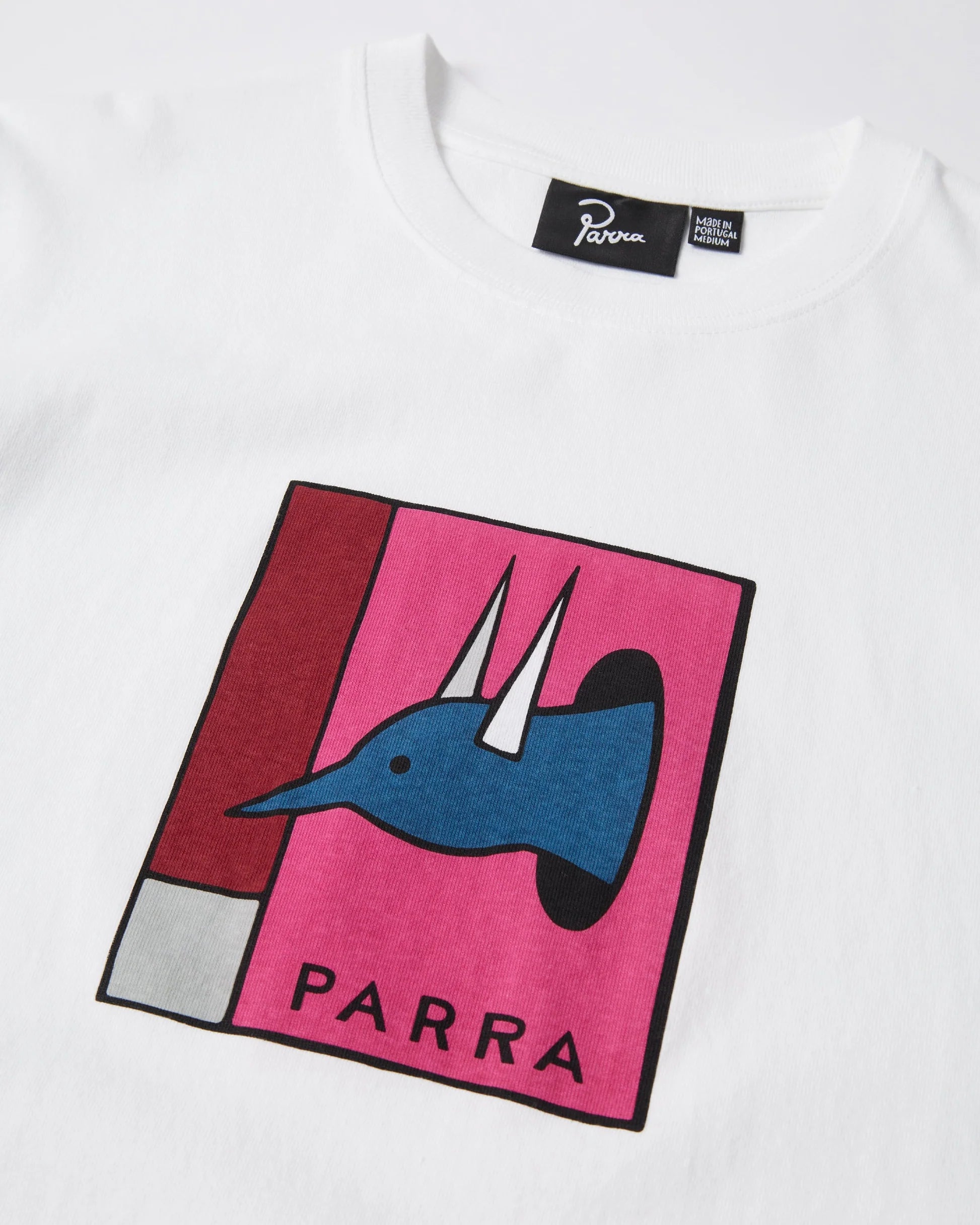 A close-up of a white crewneck t-shirt featuring a colorful graphic print of a blue character with the word 'PARRA' on a pink background, with a black Parra brand label visible inside the collar.