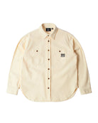 A light cream-colored long-sleeve button-up shirt with two chest pockets, laid flat against a white background. The shirt features a pointed collar, dark brown buttons, and a small black brand patch on the right chest pocket.