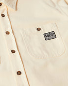 Close-up of a cream-colored button-down shirt with a chest pocket featuring a black and white 'Parra' patch.
