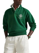 Person wearing a green sweater with a logo, standing against a white background