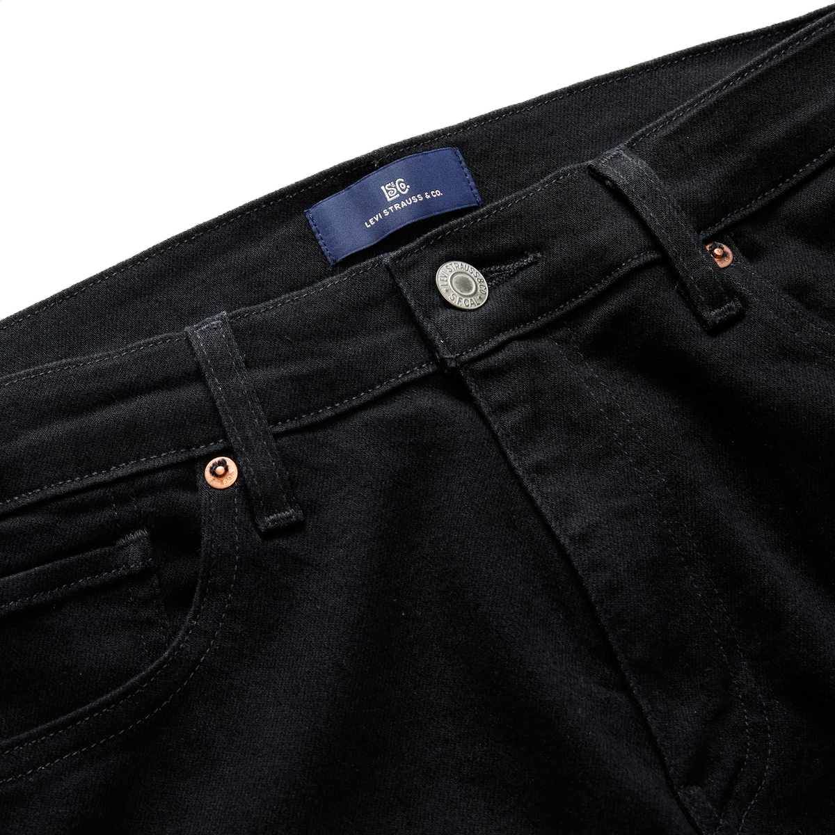Close-up of the front waistband on black Levi’s 511 Slim Jeans, with a navy Levi Strauss & Co. label, a silver shank button, and copper rivets.