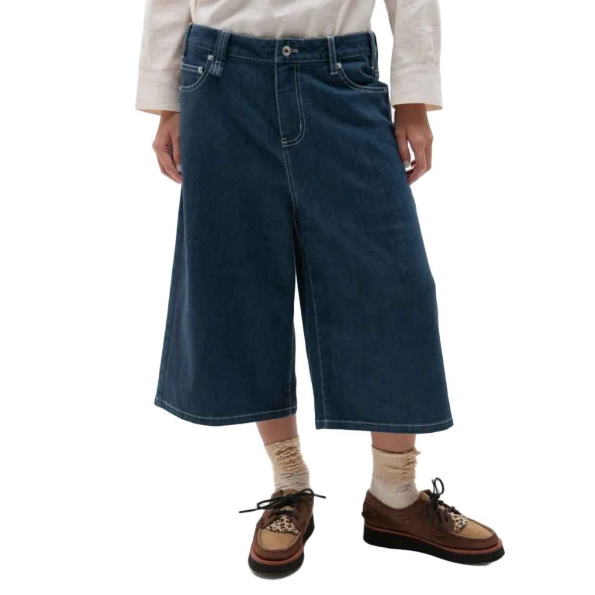 Person wearing blue wide-leg jeans, a cream shirt, brown shoes, and beige socks on a white background