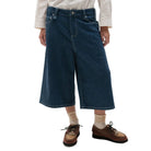 Person wearing blue wide-leg jeans, a cream shirt, brown shoes, and beige socks on a white background