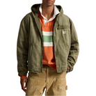 A man wearing an olive green hooded utility jacket over an orange and green striped polo shirt, paired with tan cargo pants, against a plain white background.