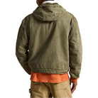 A man viewed from the back wearing an olive green hooded jacket over an orange shirt and tan pants, against a plain white background.
