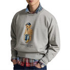 A model wears the heather gray Polo Bear sweatshirt over a plaid shirt with dark jeans. His hands are in his pockets.