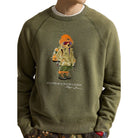 Close-up of the Polo Bear graphic on the Red Rock Crewneck: a bear in an orange beanie, ski goggles, a khaki parka, camo pants and boots, with “Polo Bear by Ralph Lauren” below.