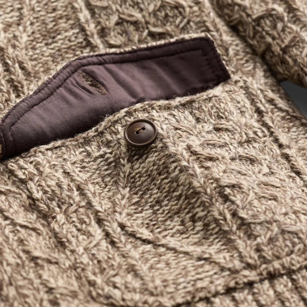 Close-up of a textured cable-knit sweater in a warm taupe-beige color, featuring a dark brown button and a matching dark brown pocket lining.