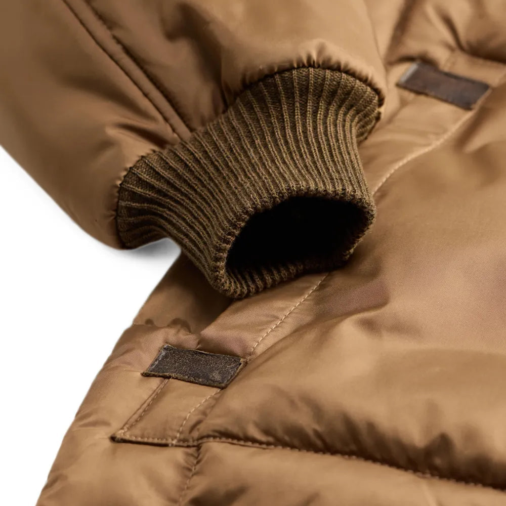 Close-up of a brown puffer jacket showing the ribbed knit cuff and a small dark label patch on the sleeve.