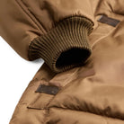 Close-up of a brown puffer jacket showing the ribbed knit cuff and a small dark label patch on the sleeve.