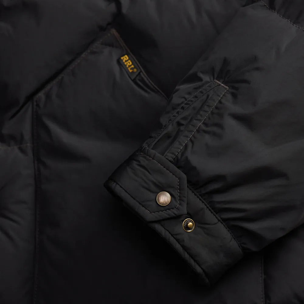 Close-up of a black puffer jacket sleeve with a buttoned cuff and a small yellow GRI brand tab near the pocket.