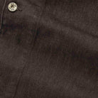 Close-up of dark brown textured fabric with a small metallic snap button at the top left corner.