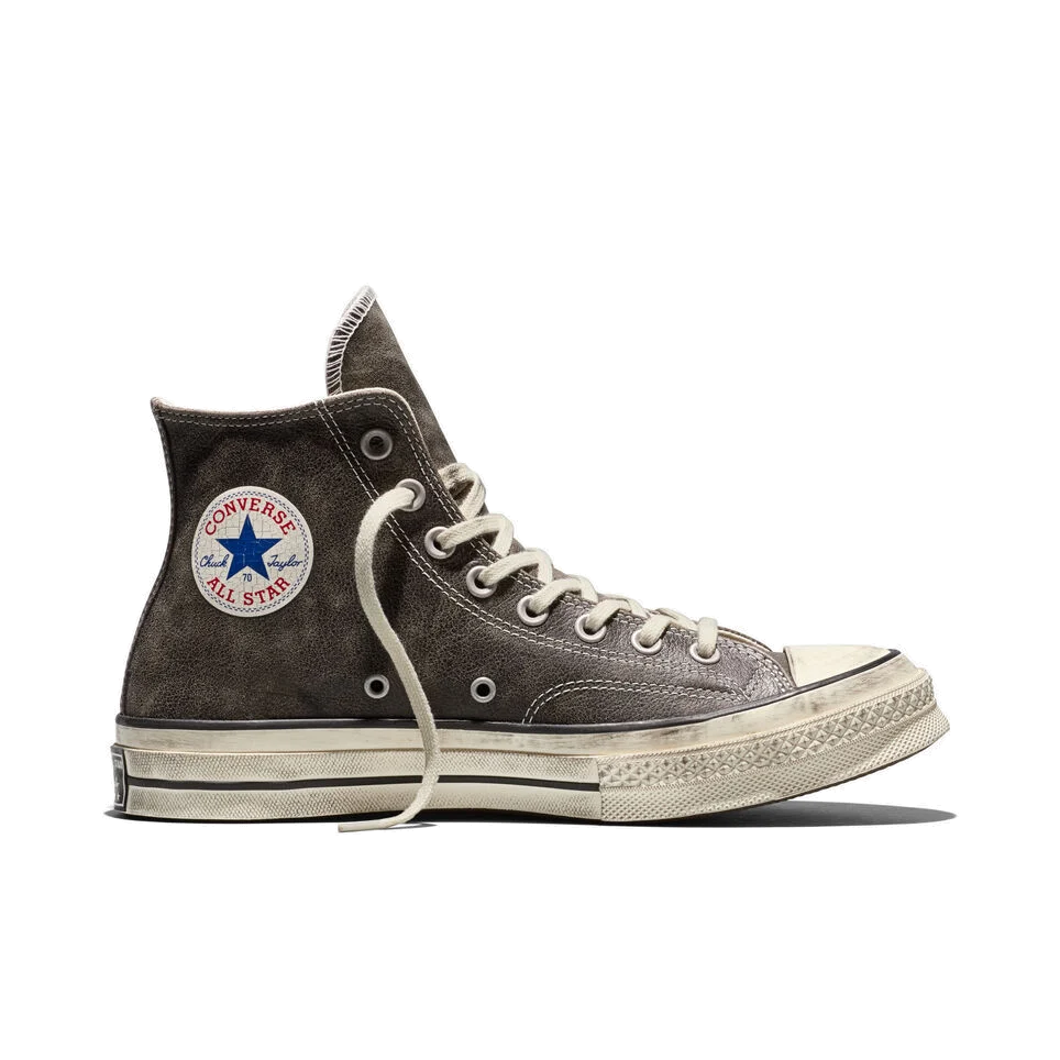 Side view of a Converse Chuck 70 high-top in faded black burnished leather, showing the Chuck Taylor All Star ankle patch, cream laces and a scuffed egret midsole.