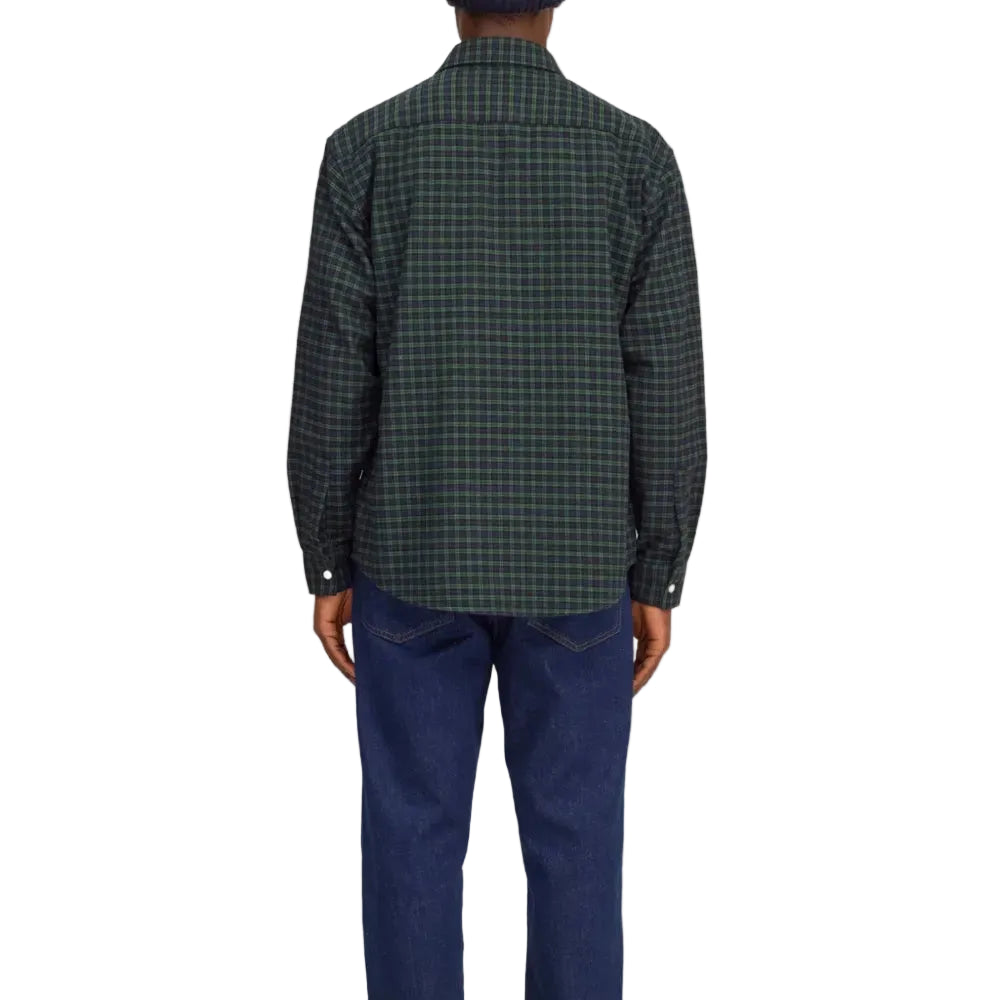 Back view of a man wearing a dark green and black Back view of plaid button-down shirt over a brown t-shirt and blue jeans, shown from the waist up against a plain white background.