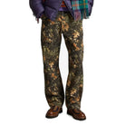 A model wears the forest-print pant with a navy puffer jacket, a plaid scarf and brown hiking boots.