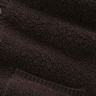 Close-up of a dark brown textured fleece with ribbed knit trim and a small button visible at the upper left.