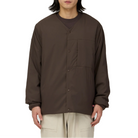 Model wearing the dark brown Snow Peak Flexible Insulated Cardigan fully snapped over a brown crewneck top, with light beige pants, showing the relaxed fit and chest pocket.