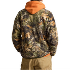 A man viewed from behind wearing a camouflage hooded jacket with a bright orange hood, a beige knit beanie, and khaki pants, set against a plain white background.