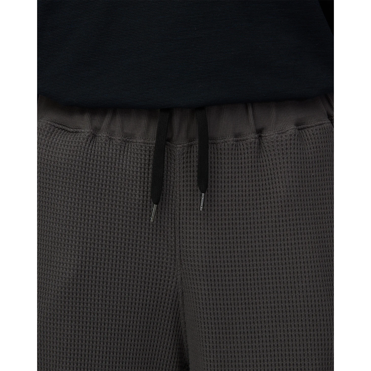 Close-up of the waistband on charcoal Snow Peak Heavyweight Waffle Pants, showing the ribbed elastic waist, black drawstring with metal tips and waffle-knit texture.