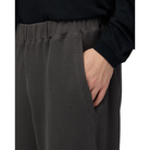 Close-up of a hand in the side pocket of charcoal Snow Peak Heavyweight Waffle Pants, showing the ribbed waistband and waffle-knit fabric.