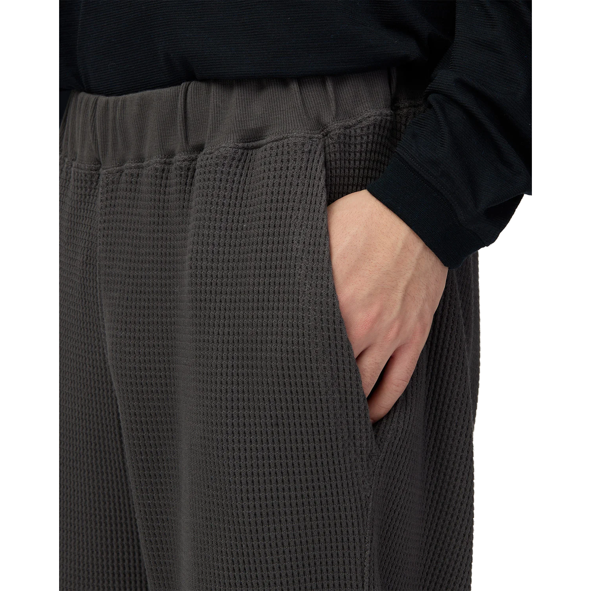 Close-up of a hand in the side pocket of charcoal Snow Peak Heavyweight Waffle Pants, showing the ribbed waistband and waffle-knit fabric.