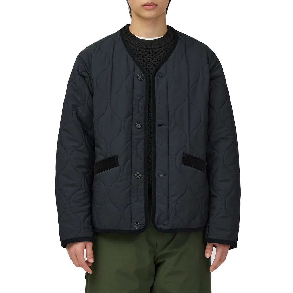Model wearing the removable quilted liner of the Snow Peak Hybrid Takibi Adjustable Jacket on its own: a collarless black button-front jacket with wavy quilting and corduroy-trimmed pockets.