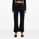A model wearing a black long-sleeve cropped button-front top and matching black wide-leg pants, paired with black pointed flats, against a plain white studio background.