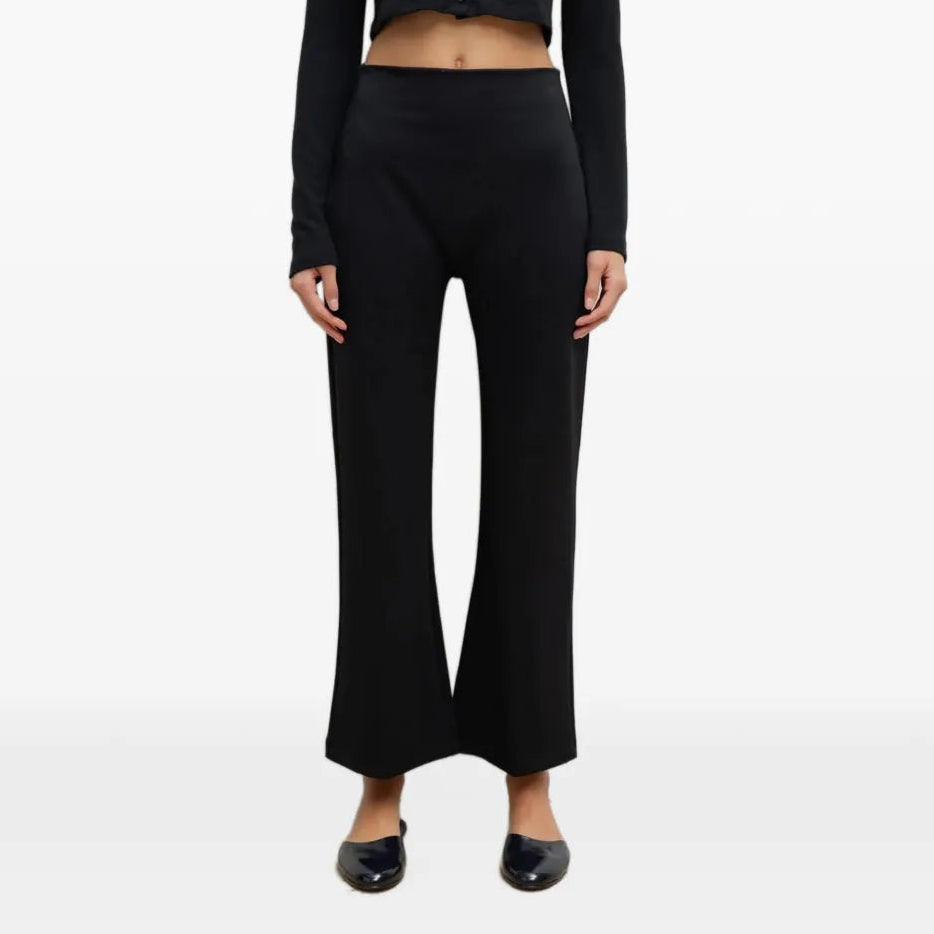 A model wearing a black long-sleeve cropped button-front top and matching black wide-leg pants, paired with black pointed flats, against a plain white studio background.