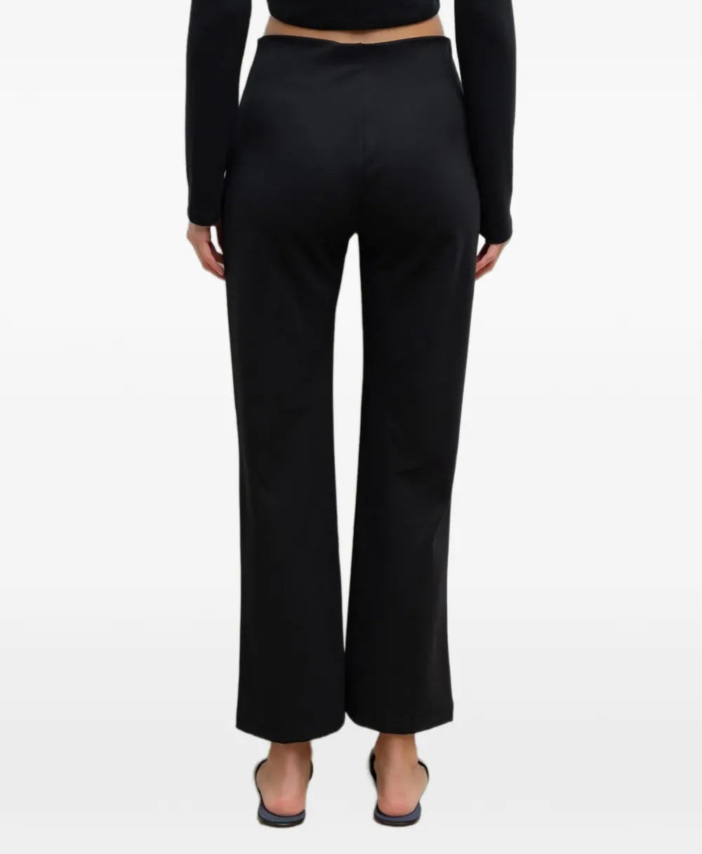 A model shown from the back wearing black wide-leg cropped pants, a black long-sleeve crop top, and black flat shoes against a plain white studio background.