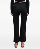 A model shown from the back wearing black wide-leg cropped pants, a black long-sleeve crop top, and black flat shoes against a plain white studio background.