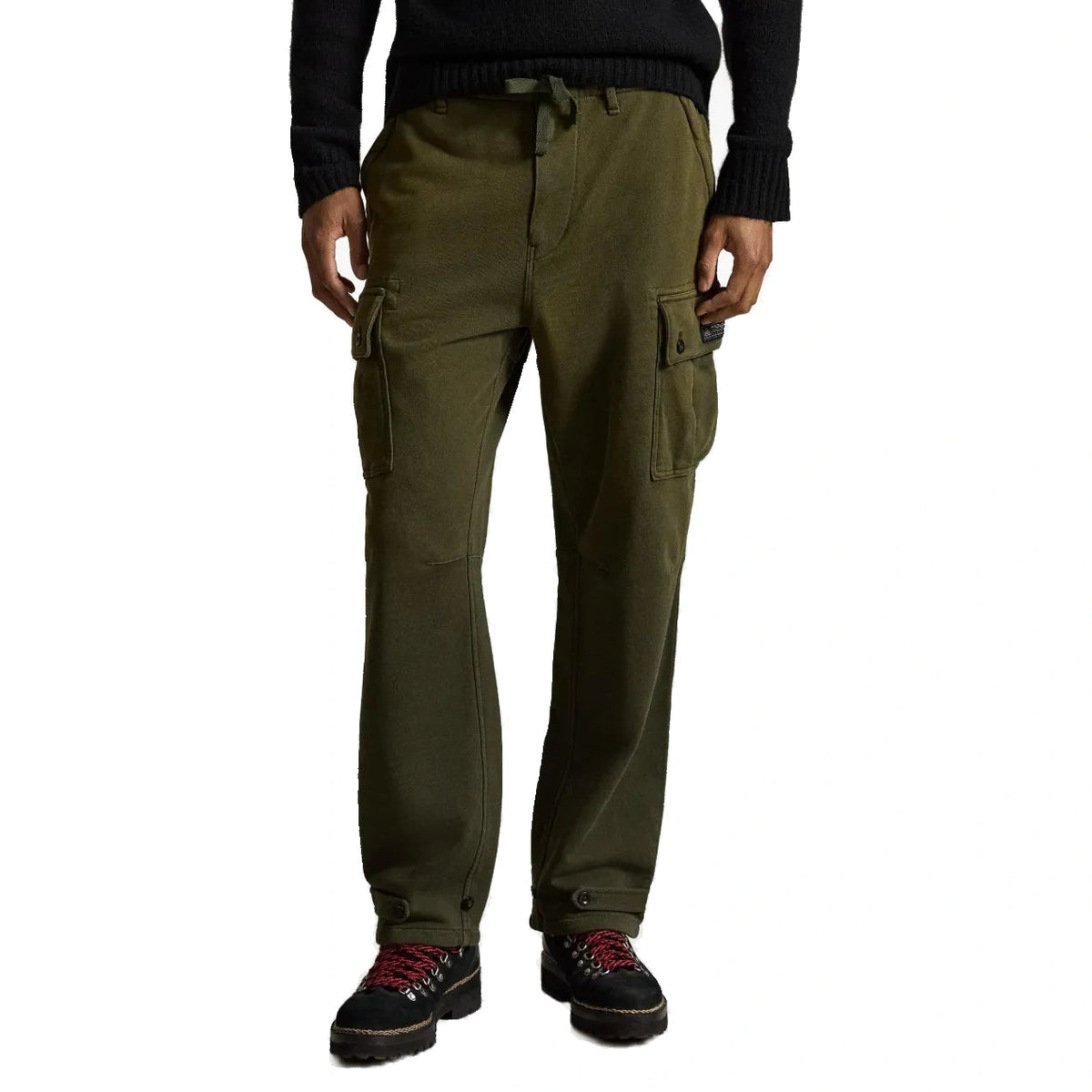 A person wearing olive green cargo pants with side flap pockets, paired with a black sweater and black shoes with red laces, shown against a plain white background.