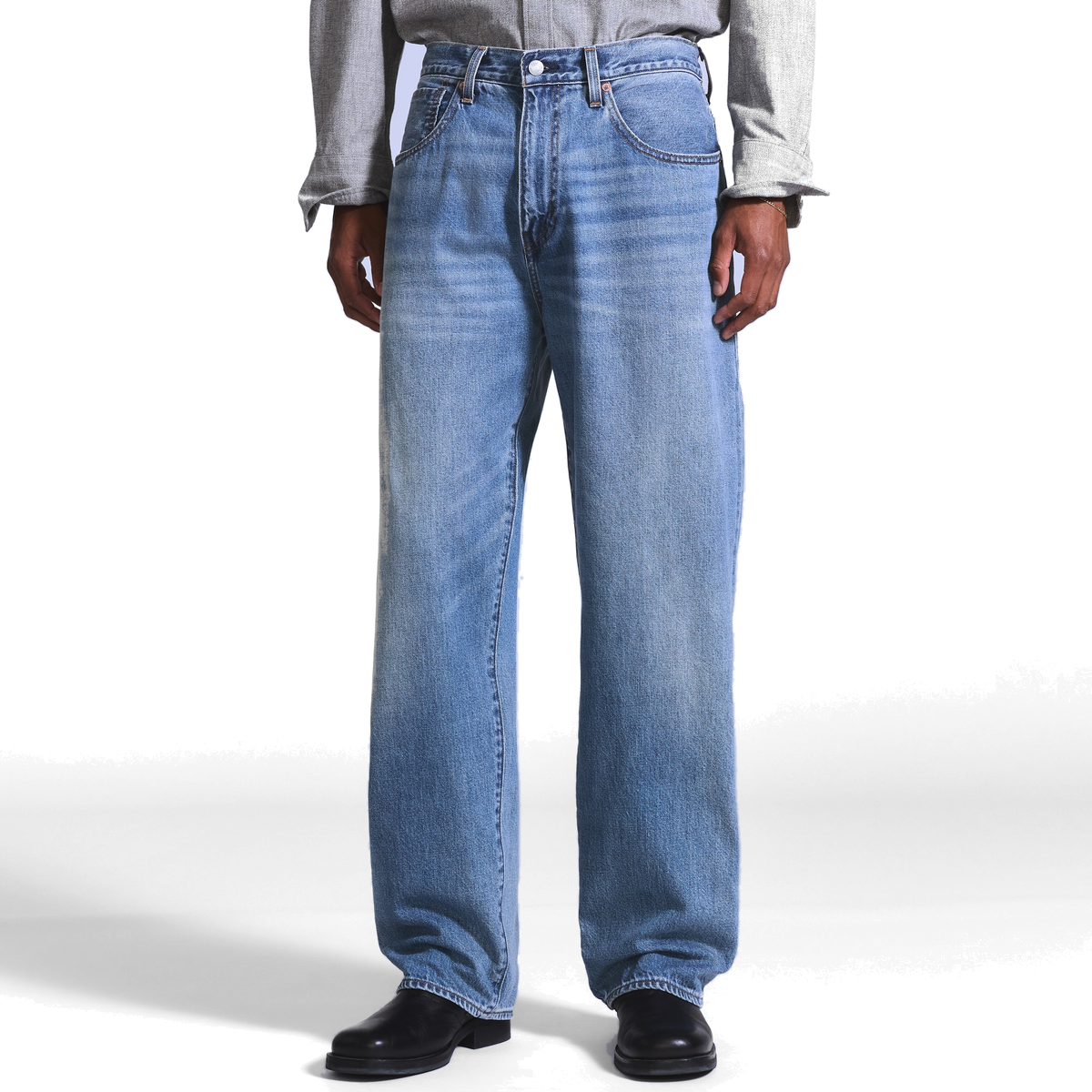Model wearing medium-wash Levi’s Marker Loose Selvedge Jeans with a grey button-up shirt and black boots, showing the loose, straight-leg fit from waist to hem.