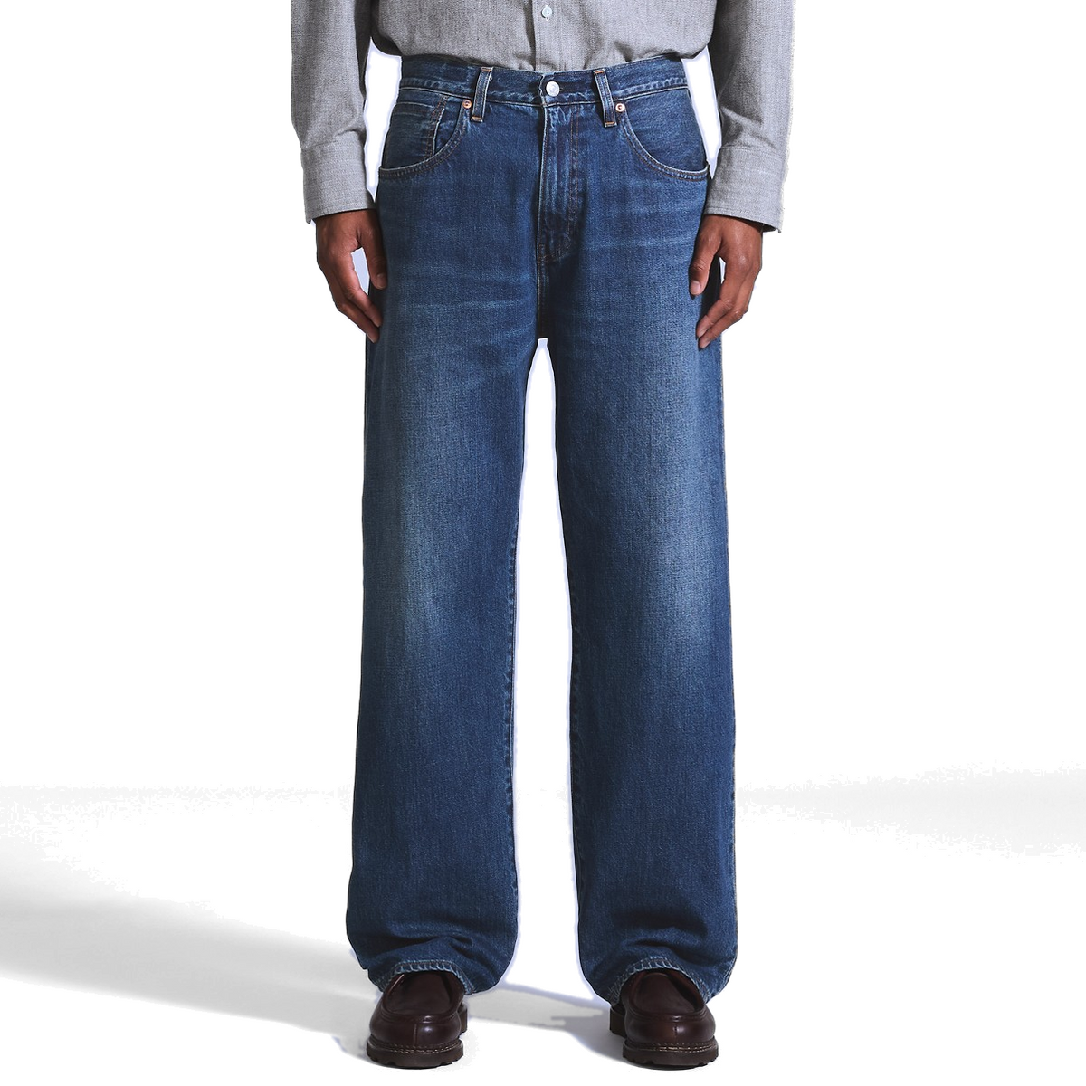 a model wearing dark indigo Levi’s Marker Loose Selvedge Jeans with a grey button-up shirt and brown leather shoes, showing the loose, straight-leg fit.