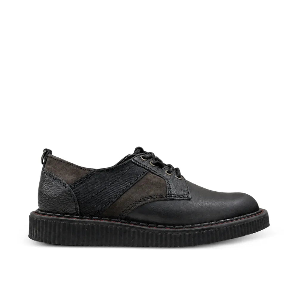 A black leather lace-up shoe with a textured panel on the side and a thick, ribbed black sole, shown from a side profile against a plain white background.