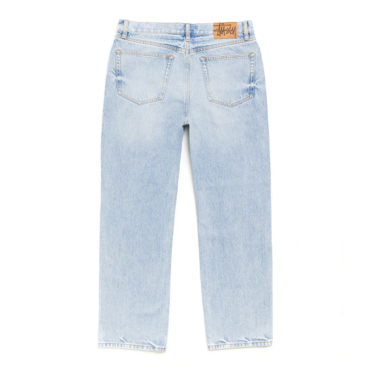 Back view of the light wash New Classic Jean laid flat, showing the two back pockets and a Stüssy leather-look patch at the waistband.
