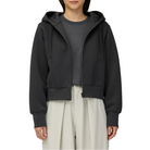 Waist-up view of a model wearing the charcoal Snow Peak Odor Control Women’s Zip Parka unzipped, showing the cropped length, drawstring hood and ribbed cuffs.