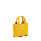 A small yellow leather handbag with double top handles, decorative gold-tone studs, and a circular embossed logo patch on the front, shown against a plain white background.