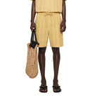 Man wearing a yellow checkered outfit holding a woven bag on a white background