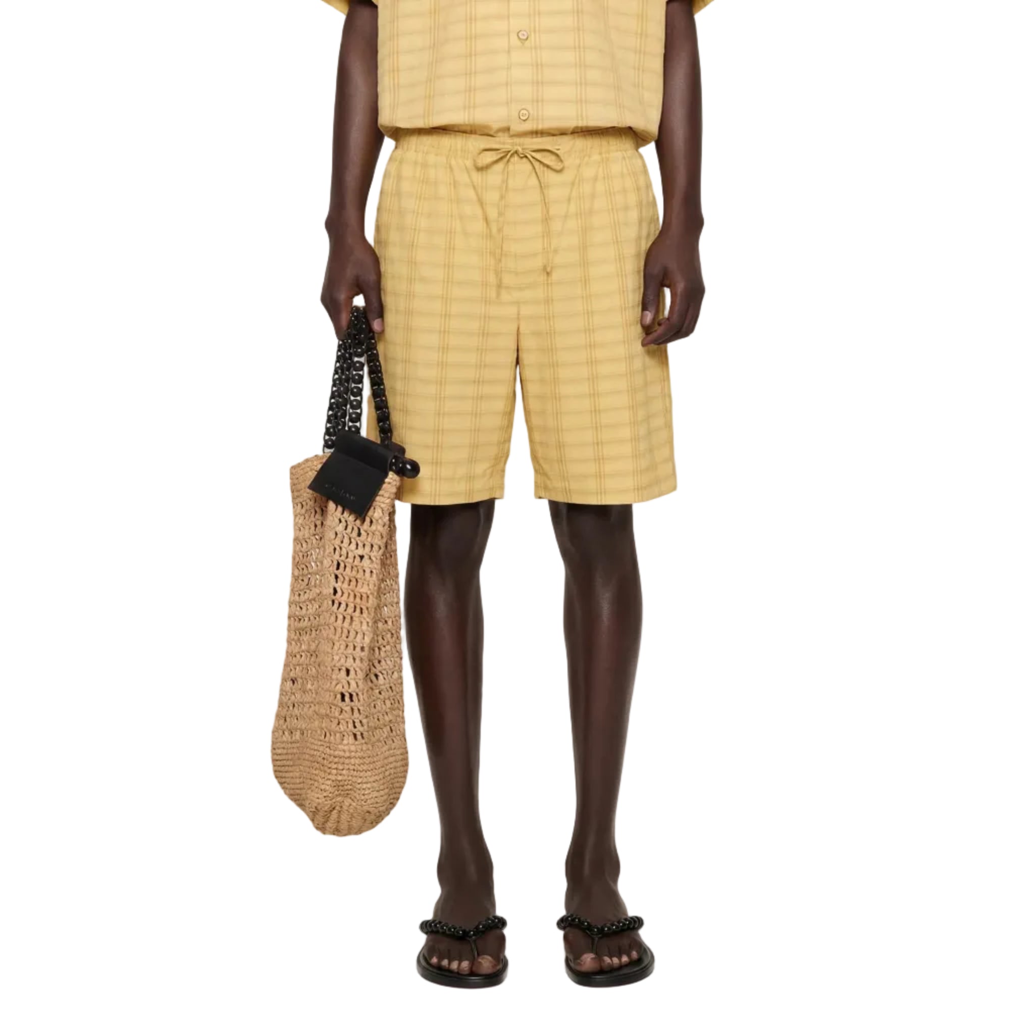 Man wearing a yellow checkered outfit holding a woven bag on a white background