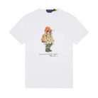 Polo Ralph Lauren Polo Bear Jersey T-Shirt laid flat. A white crewneck tee with a Polo Bear graphic in an orange beanie, ski goggles, a khaki parka and boots, with “Polo Bear by Ralph Lauren” below.