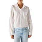 Model wearing the AMO Ruth Crop Shirt in white, slightly open at the collar, with light-wash jeans, showing the cropped, relaxed fit.