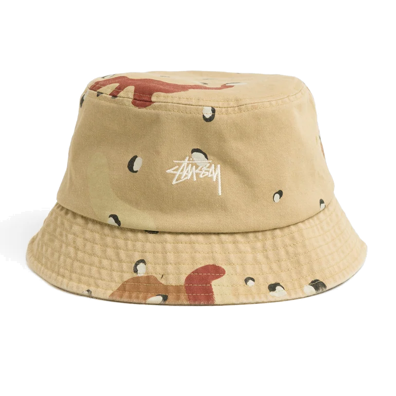 Front view of a Stüssy Stock Bucket Hat in desert camo print, with tan, brown and rust patches, black-and-white spots, and a white embroidered Stüssy logo on the crown.
