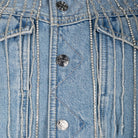 Close-up of a light blue denim jacket featuring silver beaded fringe details and decorative metal buttons.